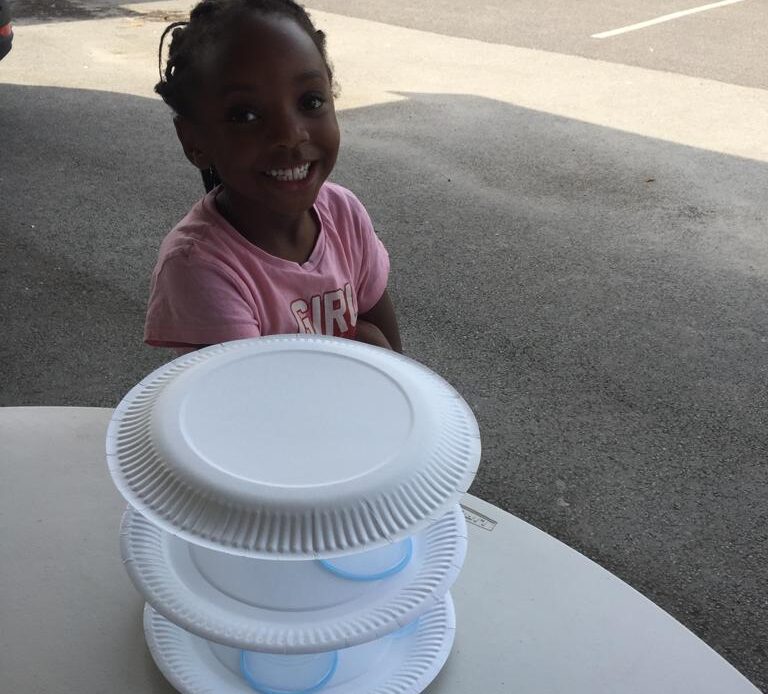 Girl smiling with a paper plate and plastic cup tower